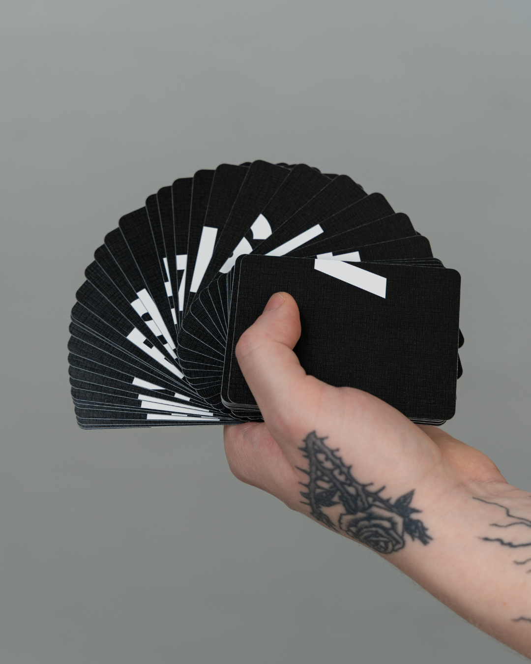 Hand holding a deck of black playing cards with white design elements against a gray background